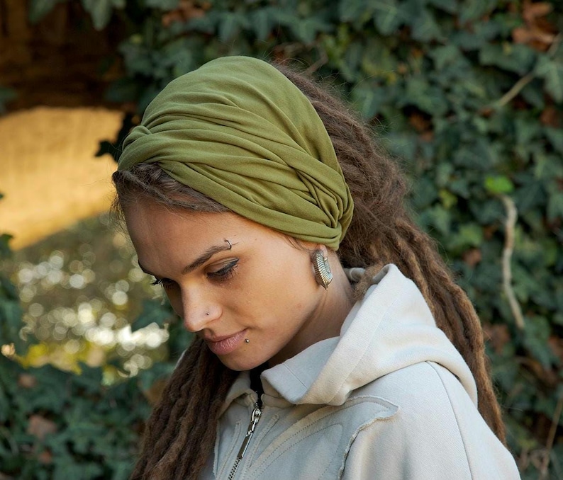 May include: An olive green fabric headband featuring a twisted knot design at the front. The headband is made of a soft, stretchy material that wraps around the head, creating a gathered, layered appearance with visible folds in the fabric.