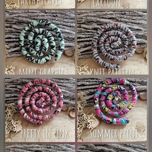 May include: A collection of spiral-shaped fabric hair accessories in various patterns and colors. Designs include "Earthy Leaves," "Cartoon," "Mint Graphic," "Knit Pattern," "Pretty in Pink," "Summer Print," "Plaid Pink," and "Night Flowers."