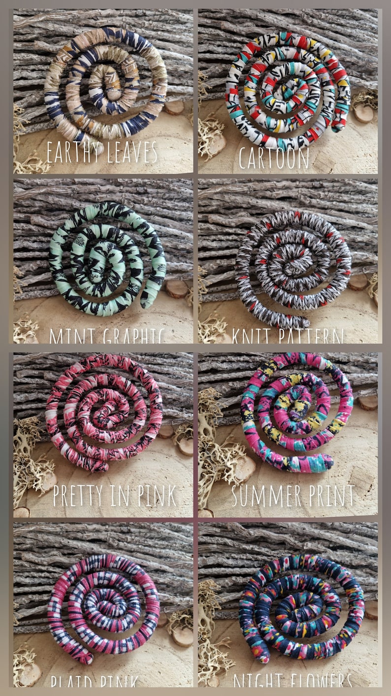 May include: A collection of spiral-shaped fabric hair accessories in various patterns and colors. Designs include "Earthy Leaves," "Cartoon," "Mint Graphic," "Knit Pattern," "Pretty in Pink," "Summer Print," "Plaid Pink," and "Night Flowers."