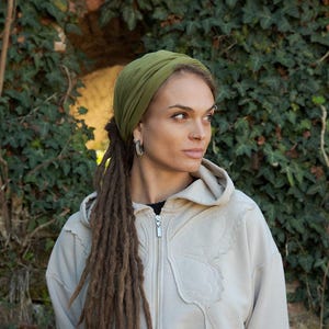 May include: A cropped beige zip-up hoodie featuring a stitched butterfly wing design on the front, paired with an olive green head wrap. The hoodie has a silver-toned zipper and a raw-edge hem, worn over a black top and light-colored bottoms.