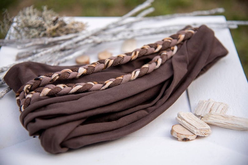 May include: A dark brown fabric headband featuring a decorative braided accent across the top. The braid is composed of three distinct strands in shades of dark brown, light tan, and a textured dark brown pattern, creating a layered appearance.