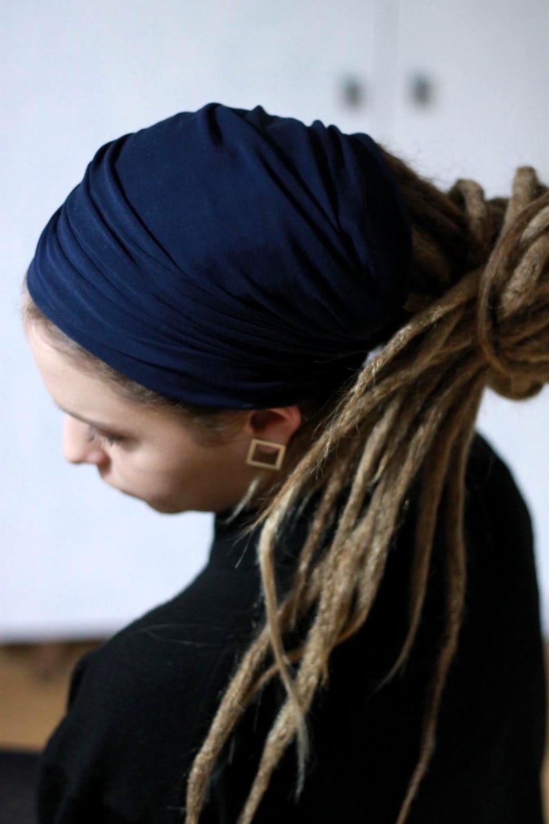 K&ouml;nnte beinhalten: Ein marineblauer Kopfwickel wird getragen. Die Person tr&auml;gt ein schwarzes Oberteil und goldene quadratische Ohrringe. Die Person hat lange, hellbraune Dreadlocks.