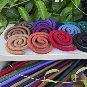 Puede incluir: Una colecci&oacute;n de cordones en espiral envueltos en tela de varios colores, incluyendo rojo, naranja, marr&oacute;n, morado, azul y negro. Las espirales est&aacute;n dispuestas sobre una superficie blanca, con longitudes rectas del mismo cord&oacute;n debajo.
