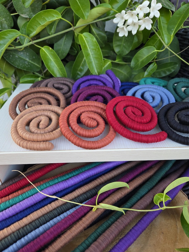 Puede incluir: Una colecci&oacute;n de cordones en espiral envueltos en tela de varios colores, incluyendo rojo, naranja, marr&oacute;n, morado, azul y negro. Las espirales est&aacute;n dispuestas sobre una superficie blanca, con longitudes rectas del mismo cord&oacute;n debajo.