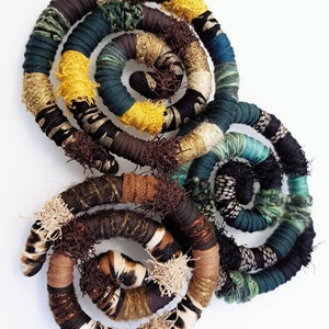 Könnte beinhalten: Ein Set aus drei gewickelten Stoffhaargummis in Braun, Grün und Gelb mit einem schwarz-weißen Zebra-Muster. Die Haargummis sind aus gewebtem Stoff und haben eine strukturierte, flauschige Optik.