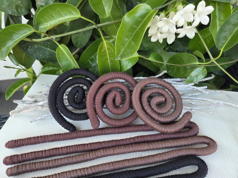 Puede incluir: Una colecci&oacute;n de formas en espiral flexibles cubiertas de tela en negro y varios tonos de marr&oacute;n. Estos objetos largos y cil&iacute;ndricos est&aacute;n enrollados en formas circulares en la parte superior, con longitudes rectas y paralelas que se extienden hacia abajo.
