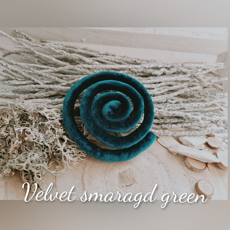 May include: A spiral-shaped object covered in dark teal velvet fabric. The item is coiled into a circular form with a smooth, soft texture. The text "Velvet smaragd green" is printed in white cursive script across the bottom of the image.