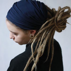 K&ouml;nnte beinhalten: Ein marineblaues Turban-Stirnband. Das Stirnband ist um den Kopf gewickelt. Die Person tr&auml;gt einen schwarzen Rollkragenpullover. Die Person hat Dreadlocks und quadratische Ohrringe.