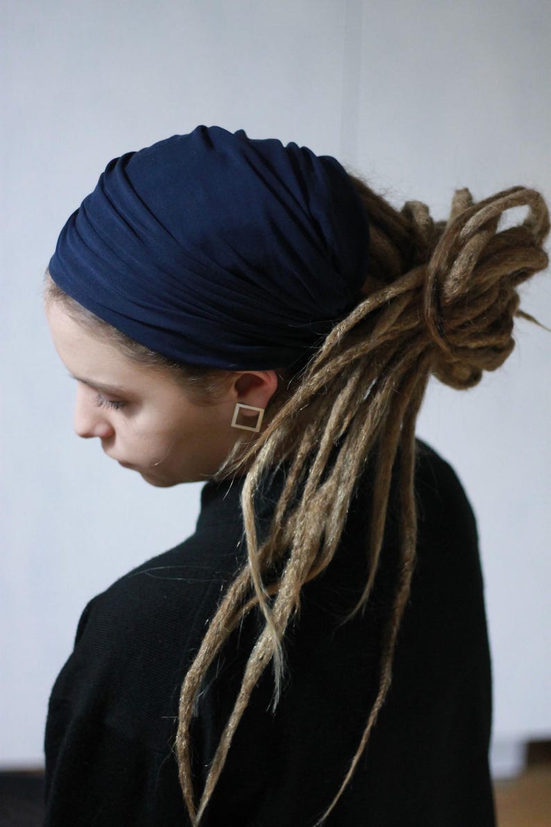 K&ouml;nnte beinhalten: Ein marineblaues Turban-Stirnband. Das Stirnband ist um den Kopf gewickelt. Die Person tr&auml;gt einen schwarzen Rollkragenpullover. Die Person hat Dreadlocks und quadratische Ohrringe.