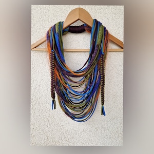 May include: A multi-colored crocheted necklace with blue, green, orange, and purple yarn. The necklace is hanging on a wooden hanger.