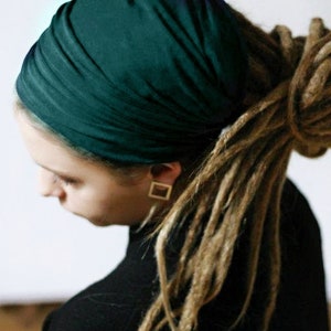 K&ouml;nnte beinhalten: Eine Person mit langen, hellbraunen Dreadlocks tr&auml;gt ein dunkelblaugr&uuml;nes Kopftuch. Die Person tr&auml;gt ein schwarzes Oberteil und goldene quadratische Ohrringe. Das Kopftuch ist aus einem weichen, drapierenden Stoff gefertigt.