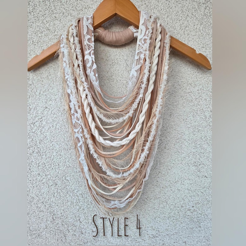 Op de afbeelding: Handgemaakte infinity sjaal in neutrale tinten, cr&egrave;me, beige en lichtbruin. De sjaal heeft verschillende texturen, zoals kant, gevlochten strengen en gefranjerde elementen. De tekst "STYLE 4" is zichtbaar aan de onderkant.