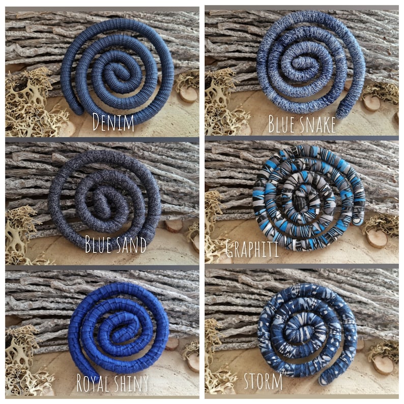 May include: Six spiral-shaped hair accessories in various shades of blue and gray. Each accessory is labeled with a descriptive name: Denim, Blue Snake, Blue Sand, Graphiti, Royal Shiny, and Storm. The accessories are displayed on a textured, neutral background.