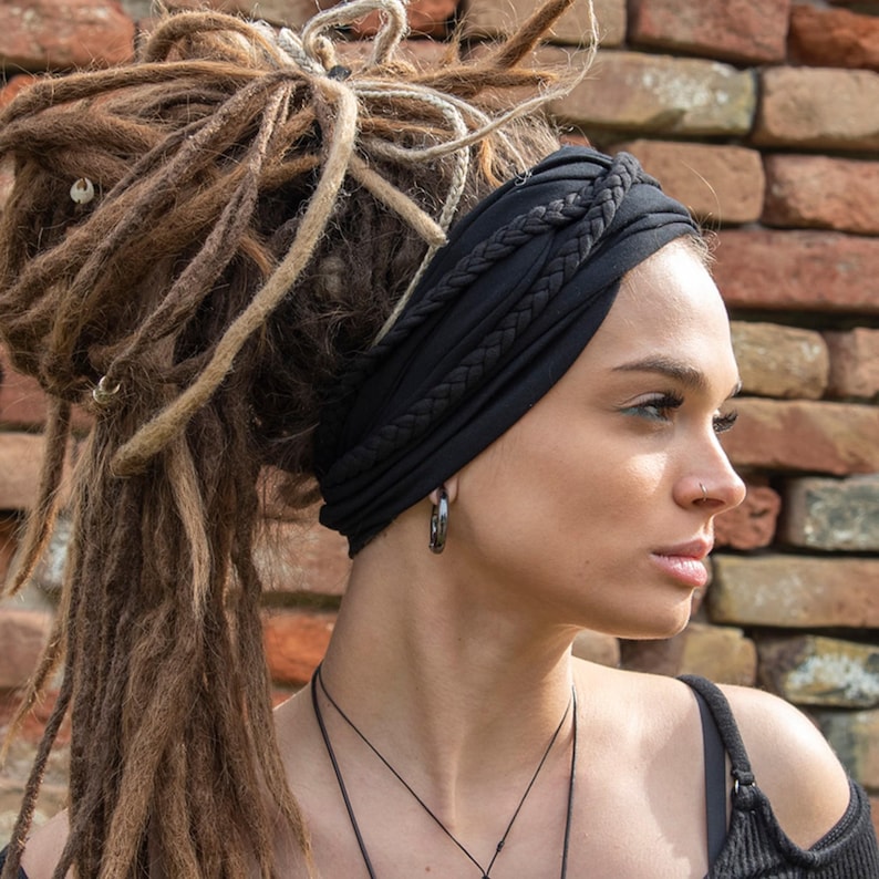 May include: A black fabric headband featuring a braided design across the top. The headband is worn around the head, positioned over the forehead and ears, and is made of a smooth, solid-colored material that stretches to fit securely.