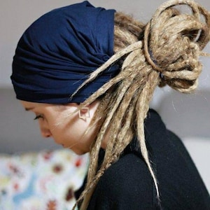 K&ouml;nnte beinhalten: Eine Person tr&auml;gt ein marineblaues Kopftuch mit langen, blonden Dreadlocks, die zu einem Dutt frisiert sind. Die Person tr&auml;gt ein schwarzes Oberteil. Der Hintergrund ist hellgrau.