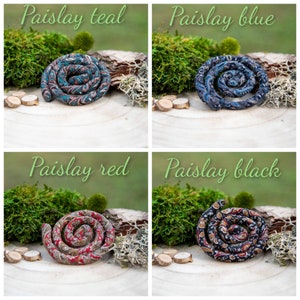 May include: Four fabric coils arranged in a spiral shape, each featuring a distinct paisley pattern in teal, blue, red, and black. The textile items are displayed with labels reading Paislay teal, Paislay blue, Paislay red, and Paislay black.