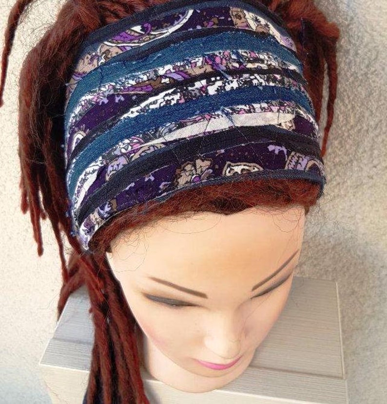 May include: A purple and blue patterned headband made of fabric strips. The headband is worn on a mannequin with long, dark red dreadlocks.