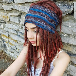 May include: A wide fabric headband featuring a dark brown base with a repeating floral pattern and horizontal bands of solid teal blue. The headband is constructed with gathered, textured fabric sections and is worn around the head.