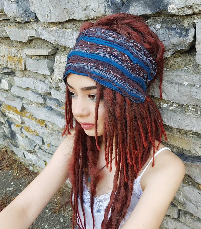May include: A wide fabric headband featuring a dark brown base with a repeating floral pattern and horizontal bands of solid teal blue. The headband is constructed with gathered, textured fabric sections and is worn around the head.
