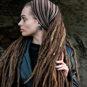 May include: A woman with long brown dreadlocks wears a brown and beige striped headband. She is wearing a black leather jacket and a black sweater.