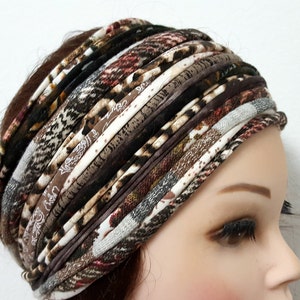 May include: A wide headband constructed from multiple strips of fabric in various brown, black, white, and tan patterns. The design features a mix of animal prints, plaid, and solid textures layered horizontally to create a thick, gathered appearance.