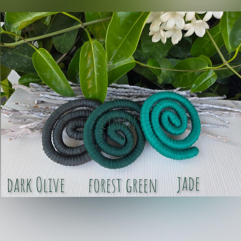 Puede incluir: Tres objetos decorativos en forma de espiral dispuestos horizontalmente, etiquetados como Dark Olive, Forest Green y Jade. Cada espiral est&aacute; construida con un material de cord&oacute;n enrollado. Los objetos se sit&uacute;an sobre un fondo de ramitas blancas.