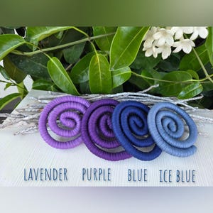 Puede incluir: Cuatro adornos en forma de espiral envueltos en tela en colores lavanda, morado, azul y azul hielo. El texto debajo de cada espiral dice: LAVENDER, PURPLE, BLUE, ICE BLUE. Estos objetos circulares est&aacute;n dispuestos sobre una superficie blanca.