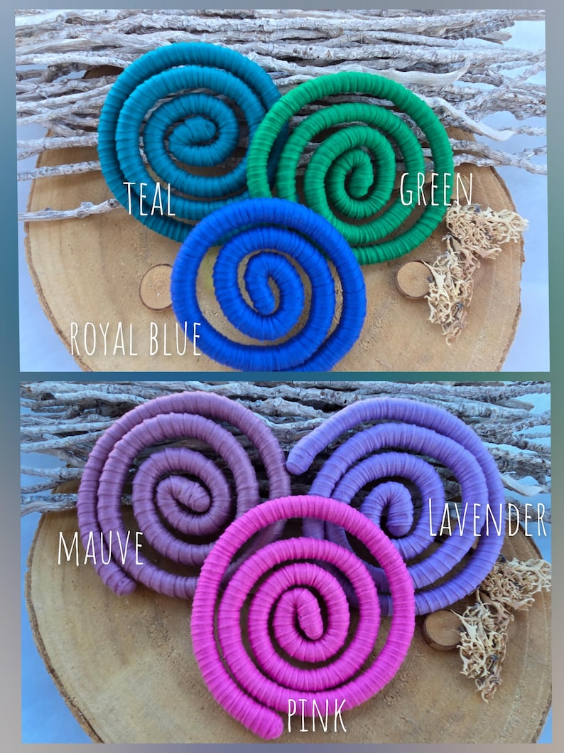 Puede incluir: Seis objetos decorativos en forma de espiral envueltos en tela, dispuestos en dos grupos. El grupo superior presenta espirales en color verde azulado, verde y azul real. El grupo inferior presenta espirales en color malva, lavanda y rosa.