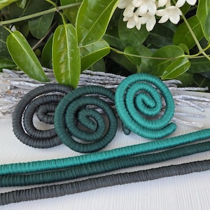 Puede incluir: Tres adornos en forma de espiral envueltos en tela, con un degradado de colores desde el gris carb&oacute;n oscuro hasta el verde bosque profundo y el azul cerceta brillante. Debajo de las espirales hay tres varillas largas y rectas de tela.