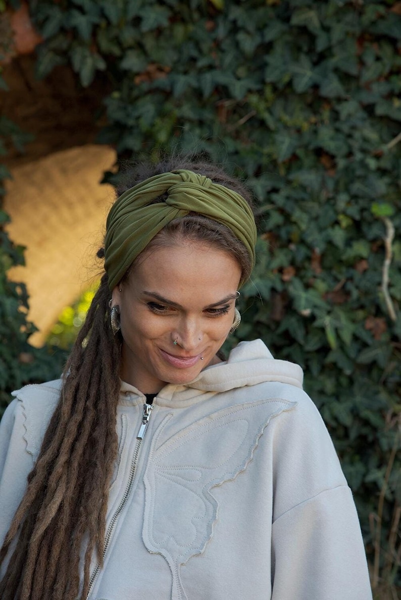 May include: An olive green fabric headband featuring a central twisted knot design. The headband is made of a soft, stretchy material and is worn across the forehead, providing a secure fit while keeping hair pulled back from the face.