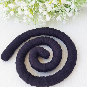 May include: A flexible, black fabric-covered coil shaped into a spiral. The material is wrapped tightly around a cylindrical core, creating a continuous, textured, and segmented appearance throughout the entire length of the dark, solid-colored object.
