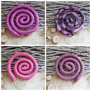 Pu&ograve; includere: Quattro accessori per capelli a forma di spirale disposti in una griglia. In alto a sinistra, fucsia lucido con texture a serpente; in alto a destra, raso fucsia con motivi neri; in basso a sinistra, tessuto rosa tinta unita; in basso a destra, tessuto color malva tinta unita.