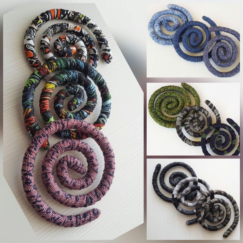 May include: A collection of spiral-shaped decorative items. The items feature fabric-covered coils in various colors and patterns, including vibrant African prints, blues, greens, and neutral tones. The spirals are arranged on a white surface.