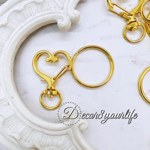 May include: Gold-colored keychains with a heart-shaped clasp and a round key ring. The keychains are displayed on a white surface with the text "Decor8 yourlife".