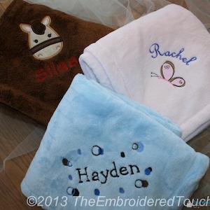 May include: Three soft, embroidered baby blankets in brown, white, and blue. The brown blanket features a horse face and the name "Silas". The white blanket has a butterfly and the name "Rachel". The blue blanket has the name "Hayden".