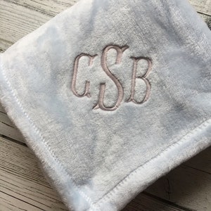 May include: A light blue plush blanket with embroidered initials "GSB" in a lighter shade. The blanket has a soft, fuzzy texture and a stitched border. The words "The Embroidered Touch" are at the bottom.