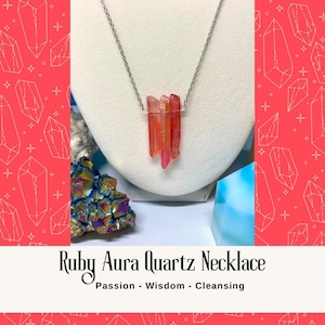 Può includere: Una collana con catena d'argento con un ciondolo fatto di più cristalli di quarzo aura rosso e arancio. La collana è su un espositore bianco. Il testo "Ruby Aura Quartz Necklace" e "Passion - Wisdom - Cleansing" è sotto l'immagine.