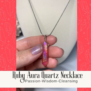 Può includere: Una collana con catena d'argento con un ciondolo in quarzo aura rosa e iridescente. Il ciondolo è una punta lunga e sottile. Il testo "Ruby Aura Quartz Necklace Passion-Wisdom-Cleansing" è sotto l'immagine.