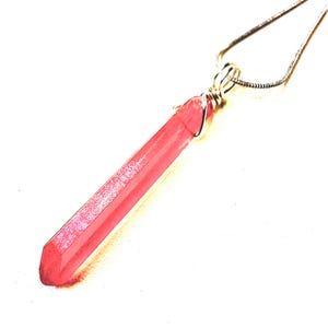 Op de afbeelding: Een roze kristallen hangerketting. De kristal heeft een lange, facetvormige vorm met een zilveren draadwikkeling en hangt aan een fijne zilveren ketting. De kristal heeft een lichte glans en is een levendige roze tint.