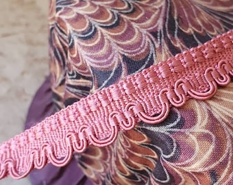 May include: Pink scalloped trim with a decorative design. The trim is made of a soft, woven fabric and has a delicate, feminine look.