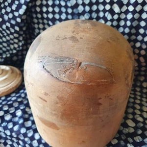 May include: A brown wooden hat block with a slightly rounded top and a smooth, worn surface.