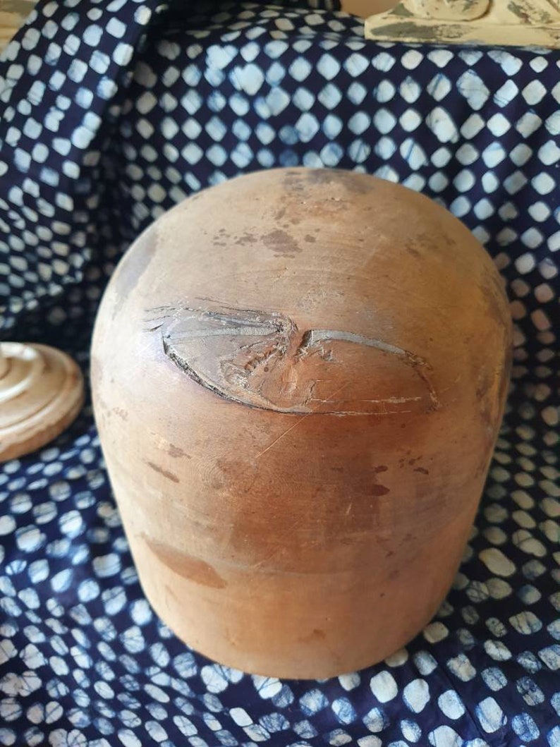 May include: A brown wooden hat block with a slightly rounded top and a smooth, worn surface.