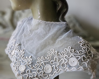 May include: A white lace collar with a delicate, intricate design. The lace is made of a fine mesh with a scalloped edge. The collar is perfect for adding a touch of vintage elegance to any outfit.