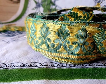 May include: Green and gold trim with a floral pattern. The trim is woven and has a slightly frayed edge.