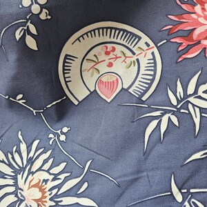 May include: Close-up of a fabric with a repeating floral pattern. The design features large pink and white flowers, cream-colored leaves, and stylized fan-shaped elements with red berries, all set against a muted blue background.
