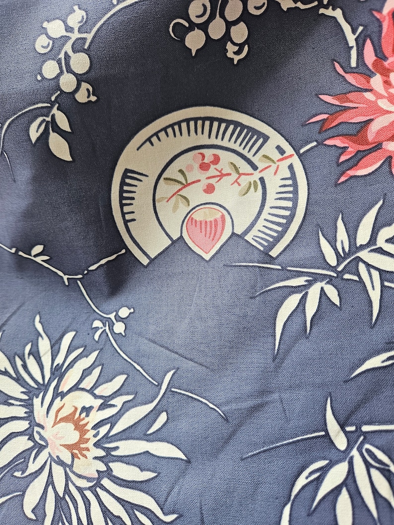 May include: Close-up of a fabric with a repeating floral pattern. The design features large pink and white flowers, cream-colored leaves, and stylized fan-shaped elements with red berries, all set against a muted blue background.
