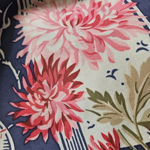 May include: Close-up of a fabric with a floral pattern. The design features large pink and red chrysanthemum flowers, green leaves, and white accents on a navy blue background. The fabric has a vintage or retro aesthetic.