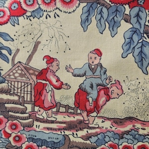 Peut inclure: Gros plan sur un tissu avec une scène pastorale. Le motif présente des personnages vêtus de rouge et de bleu, un petit bâtiment et des éléments floraux et de feuillage rouges, roses et bleus sur fond crème.