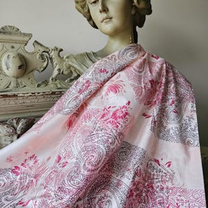May include: A pink and white paisley patterned fabric with a black outline. The fabric is draped over a plaster bust of a woman.