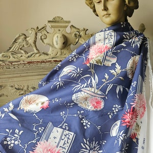 May include: A piece of blue fabric with a floral pattern featuring pink and white flowers, bamboo, and Japanese characters. The fabric is draped over a statue's shoulders. The fabric has a white edge with text.